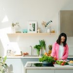 A woman in pink prepares fresh vegetables in a sunlit, modern kitchen, creating a vibrant cooking scene.